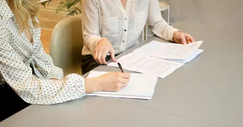 Two people at a table, one signing a document