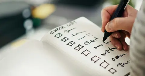 Hand ticking boxes on a handwritten checklist in a notebook