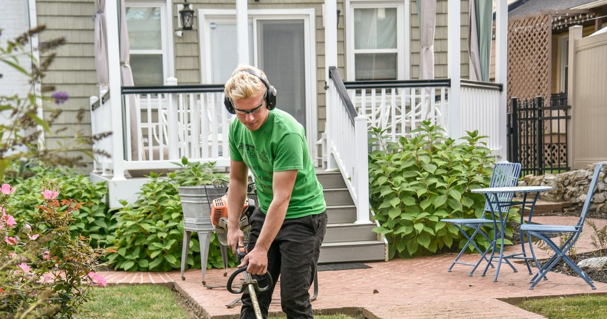 Landscaper trimming the edge of a lawn in front of a house