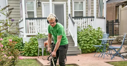 Landscaper trimming the edge of a lawn in front of a house